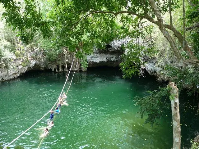 Tourists enjoying a zipline ride over a natural cenote surrounded by lush greenery in Cancun.