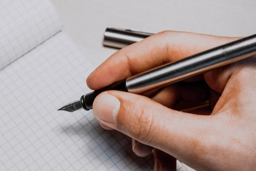 Writing with the Grafton Pen Person writing on a paper notebook with a metal aluminum pen
