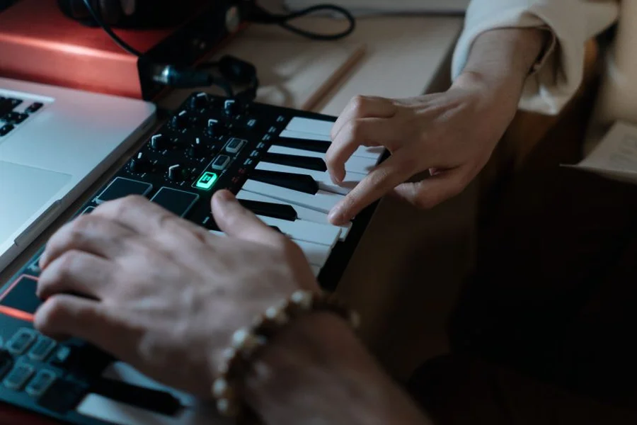 Musician playing keyboard connected via midi to usb lead to a laptop recording studio